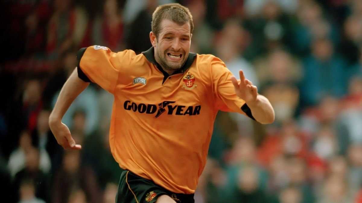 Steve Bull - THEWILL NEWS MEDIA Athlete in an orange jersey sprinting on a field with a blurred crowd in the background, sponsor logo on chest.