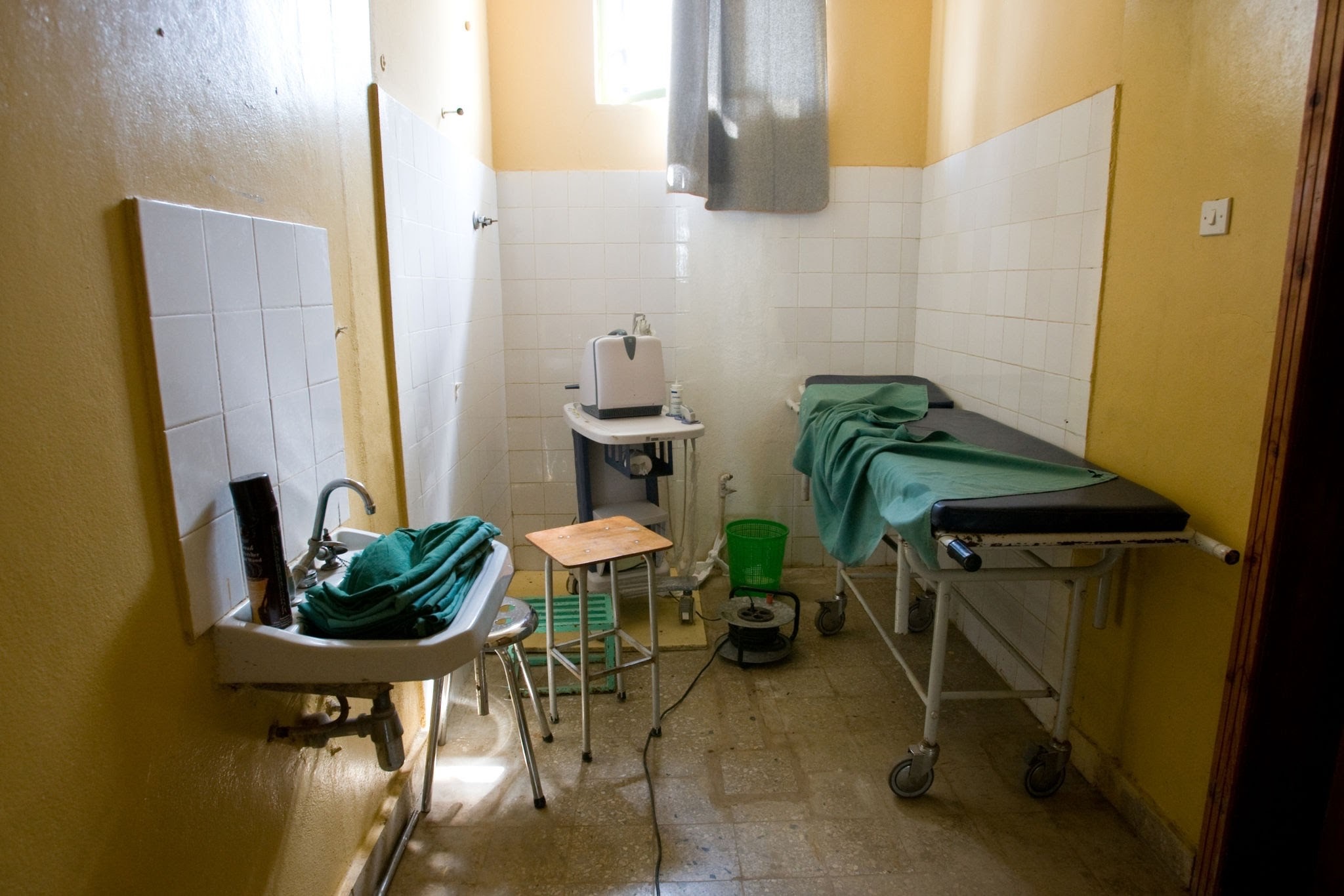 Treatment room - THEWILL NEWS MEDIA Small medical examination room with a green-covered table, sink, and medical equipment against pale yellow walls