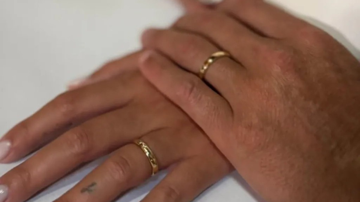 Wedding ring - THEWILL NEWS MEDIA Close-up of two hands wearing gold wedding bands, one resting atop the other on a light surface.