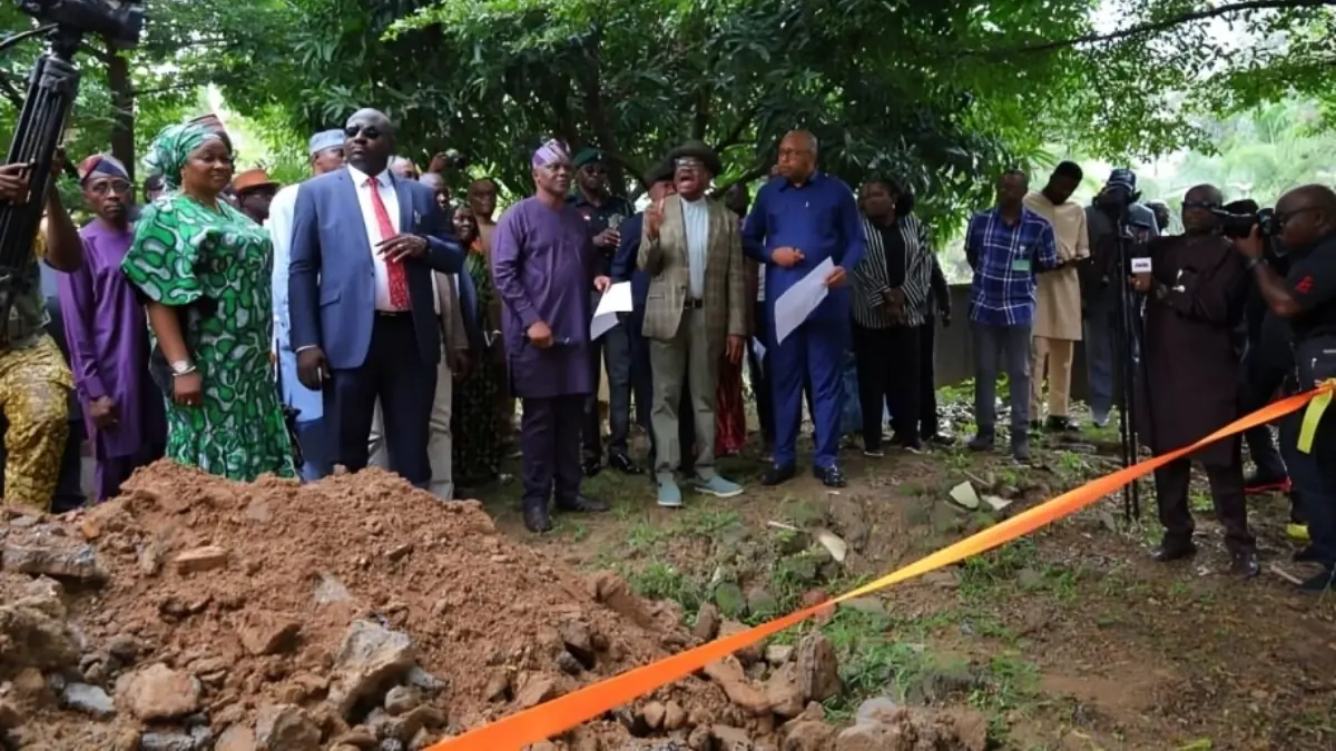 Wike and officials inspect an area affected by flooding - THEWILL NEWS MEDIA Dignitaries and reporters attend a ground-breaking ceremony with an orange ribbon and dirt mound in a green, outdoor setting.