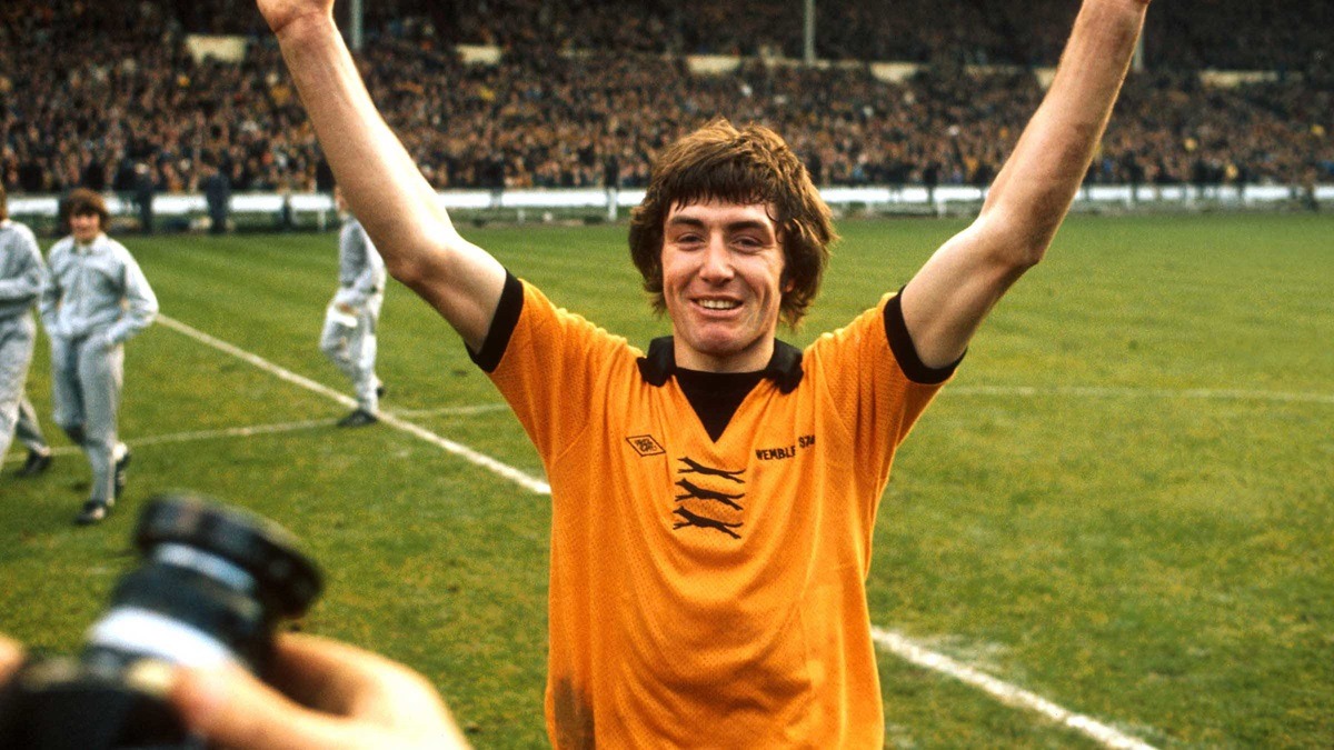 john-richards - THEWILL NEWS MEDIA Soccer player in an orange jersey raises both arms in celebration on a grassy field with a cheering crowd in the background.
