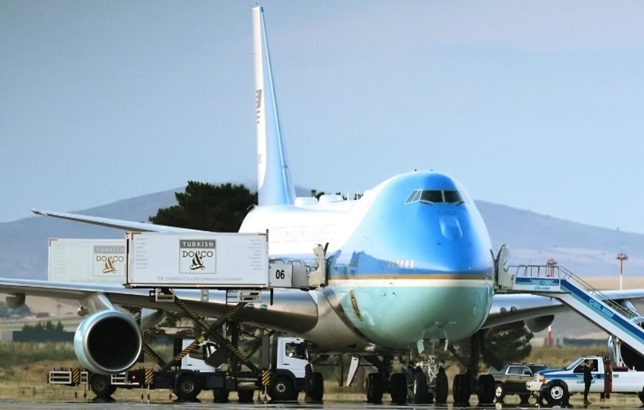 older Air Force One - THEWILL NEWS MEDIA Wide-body cargo airplane with blue nose parked on the tarmac, pallets being loaded and ground vehicles nearby
