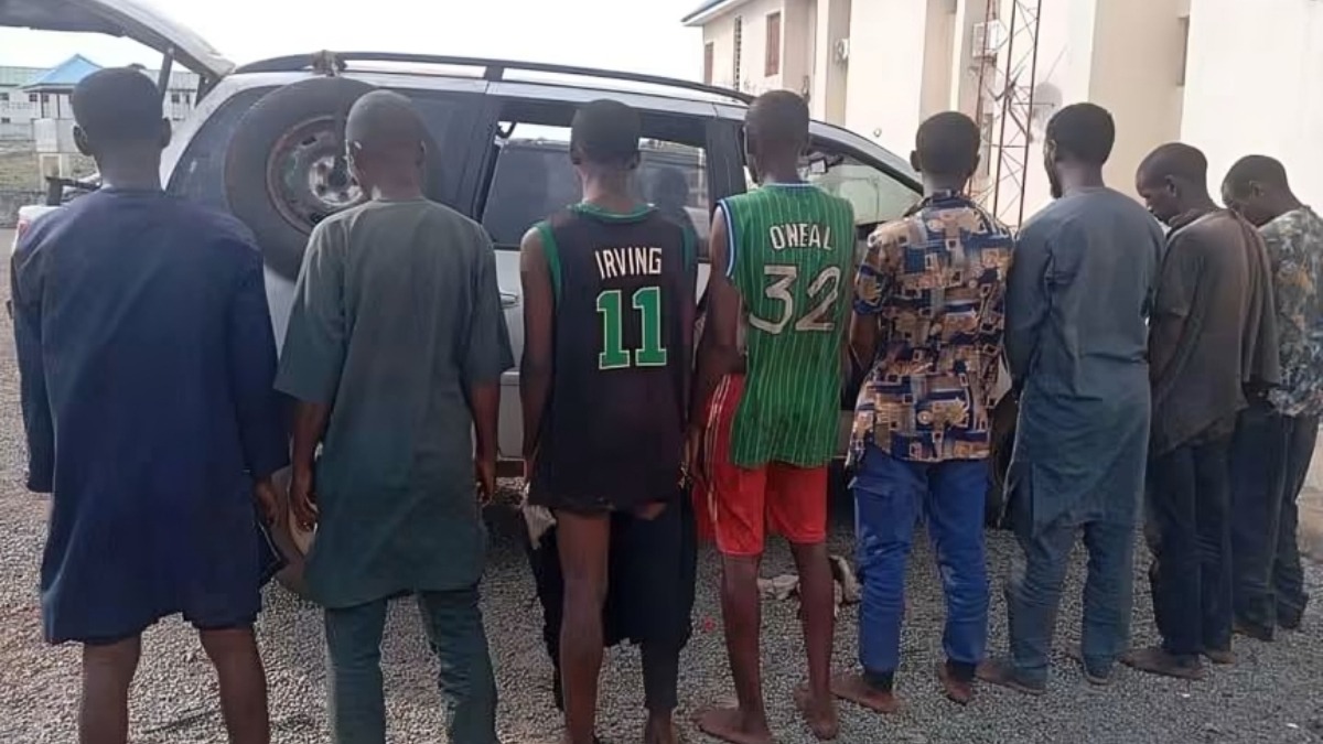 suspected kidnappers - THEWILL NEWS MEDIA A line of men in casual clothes stands behind a silver SUV with its rear hatch open, looking at the vehicle.