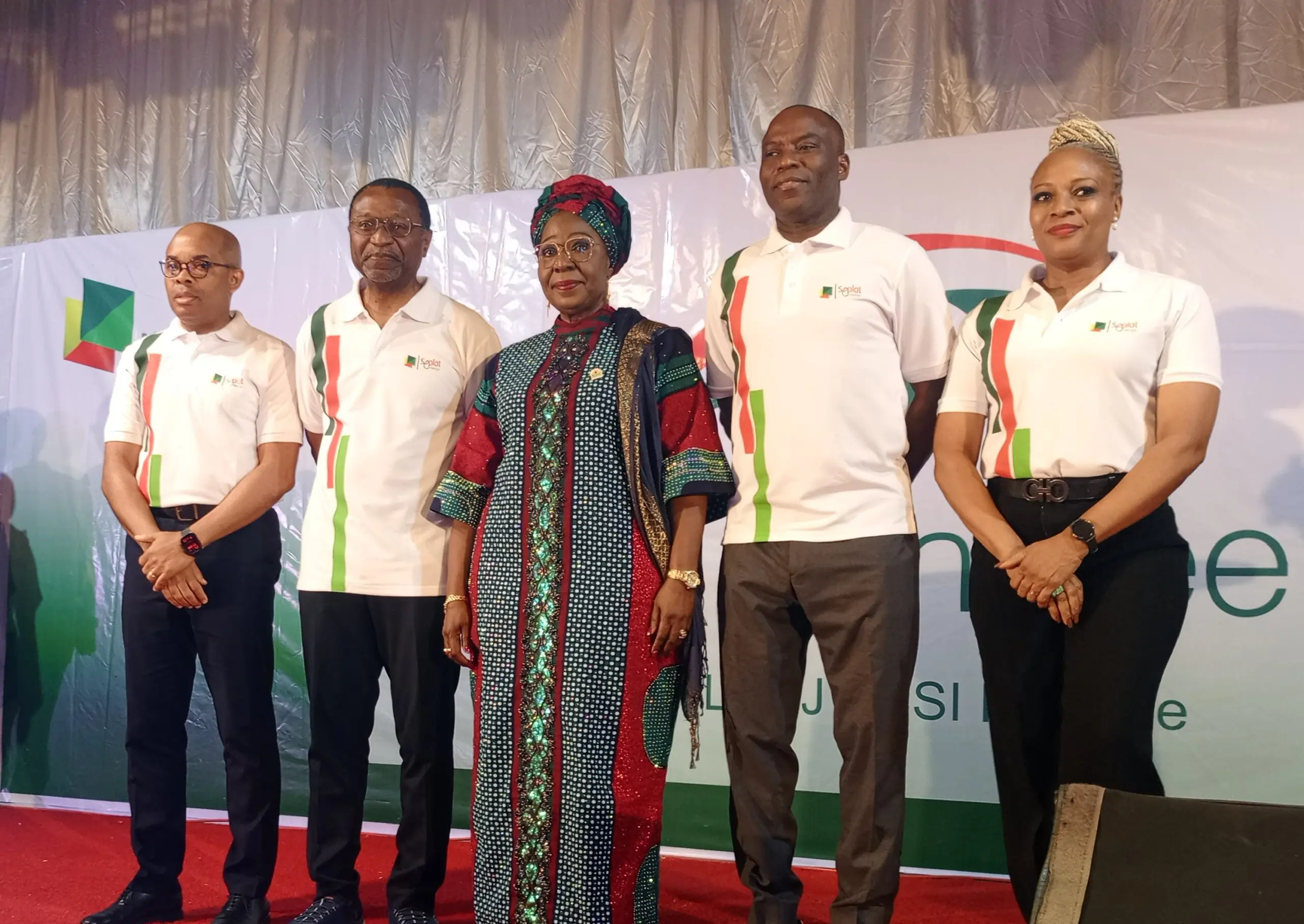 Seplat Energy Eye Programme In Akwa Ibom - THEWILL NEWS MEDIA Group of five people posing on a stage, four in white polo shirts with green and red accents and one woman in colorful traditional dress and head wrap.