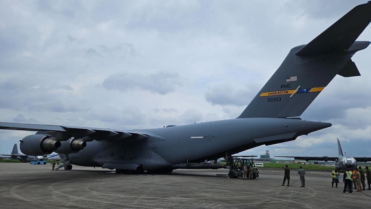 A US Air Force C-17 military transport aircraft flew - THEWILL NEWS MEDIA Gray USAF C-17 Globemaster III cargo aircraft on a tarmac, tail marked AMC Charleston 00213, with ground crew nearby and other aircraft in the background.