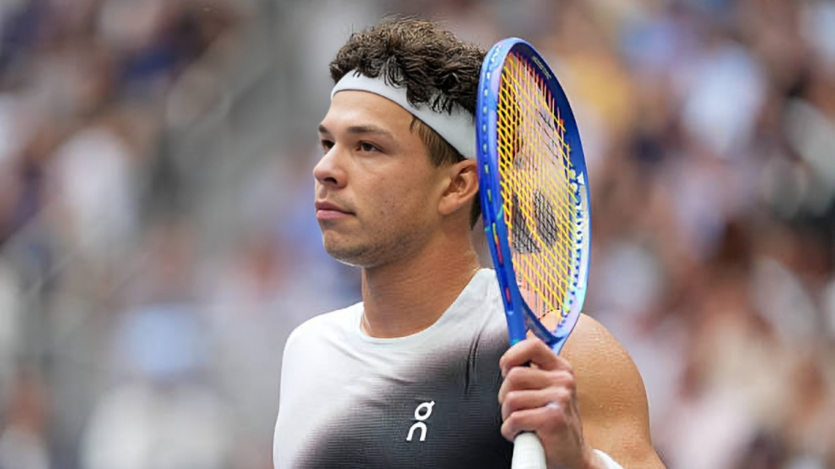Ben Shelton - THEWILL NEWS MEDIA Male tennis player in a sleeveless top holding a blue racquet, looking off to the side during a match Surrounded by a blurred crowd.