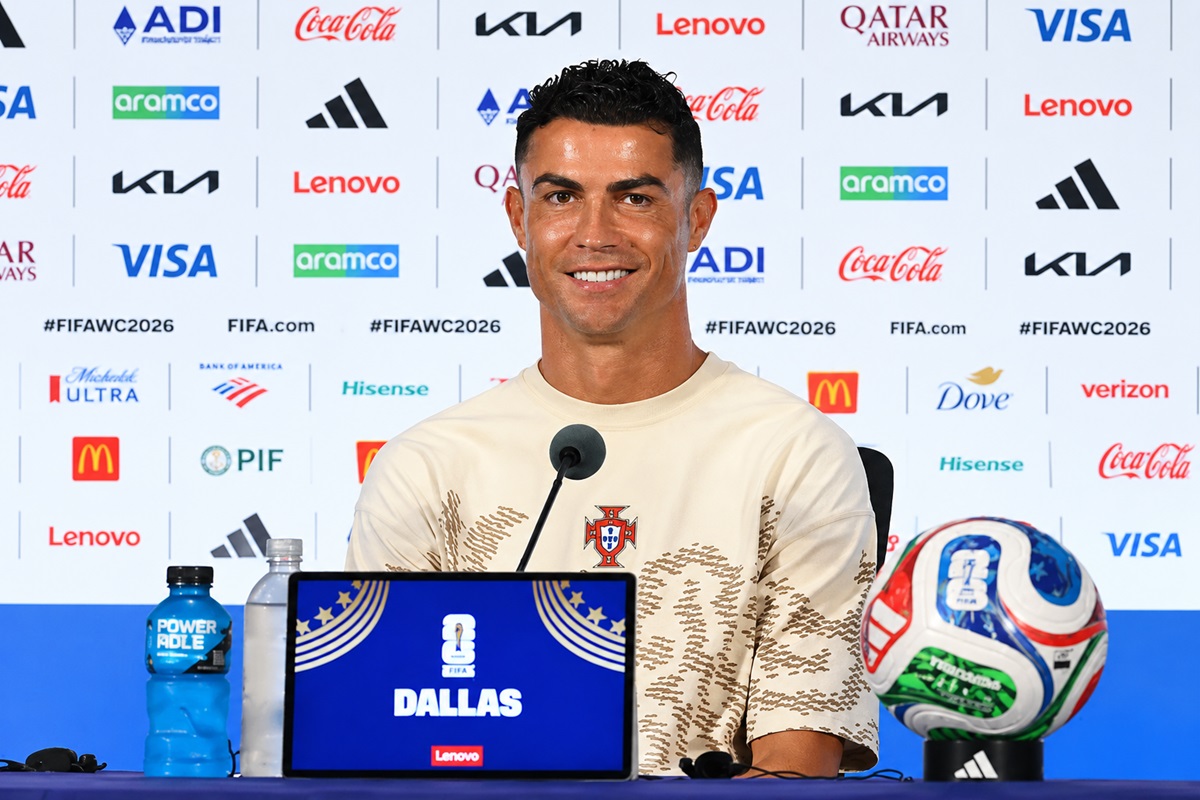 Cristiano Ronaldo - THEWILL NEWS MEDIA Male footballer at a press conference; Portugal crest on shirt, Dallas FIFA signage, microphone, and a soccer ball nearby.