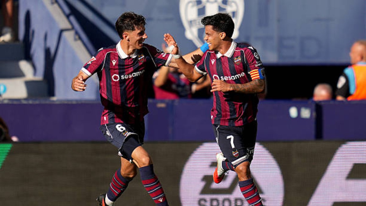 Levante - THEWILL NEWS MEDIA Two soccer players in maroon and navy striped uniforms celebrate on the field, high-fiving as they run after a goal.