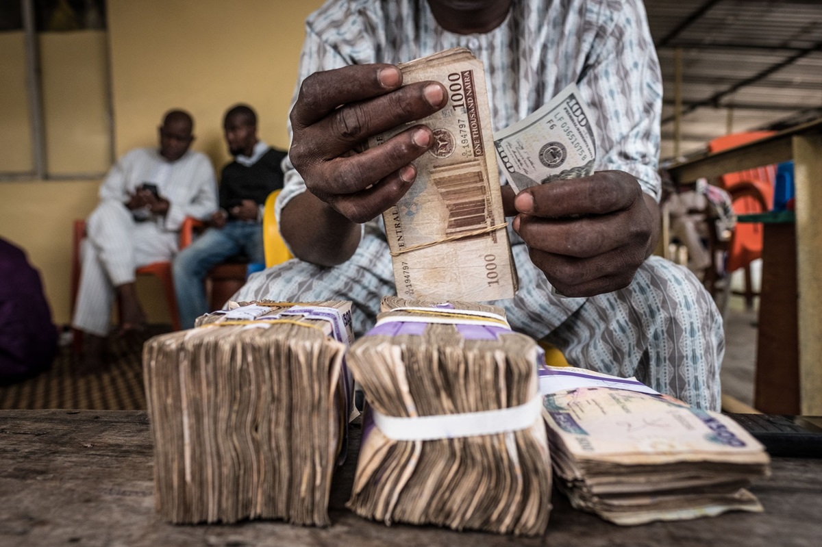 Naira notes - THEWILL NEWS MEDIA Man counting a stack of cash, with several bundles laid out on a wooden table in the foreground
