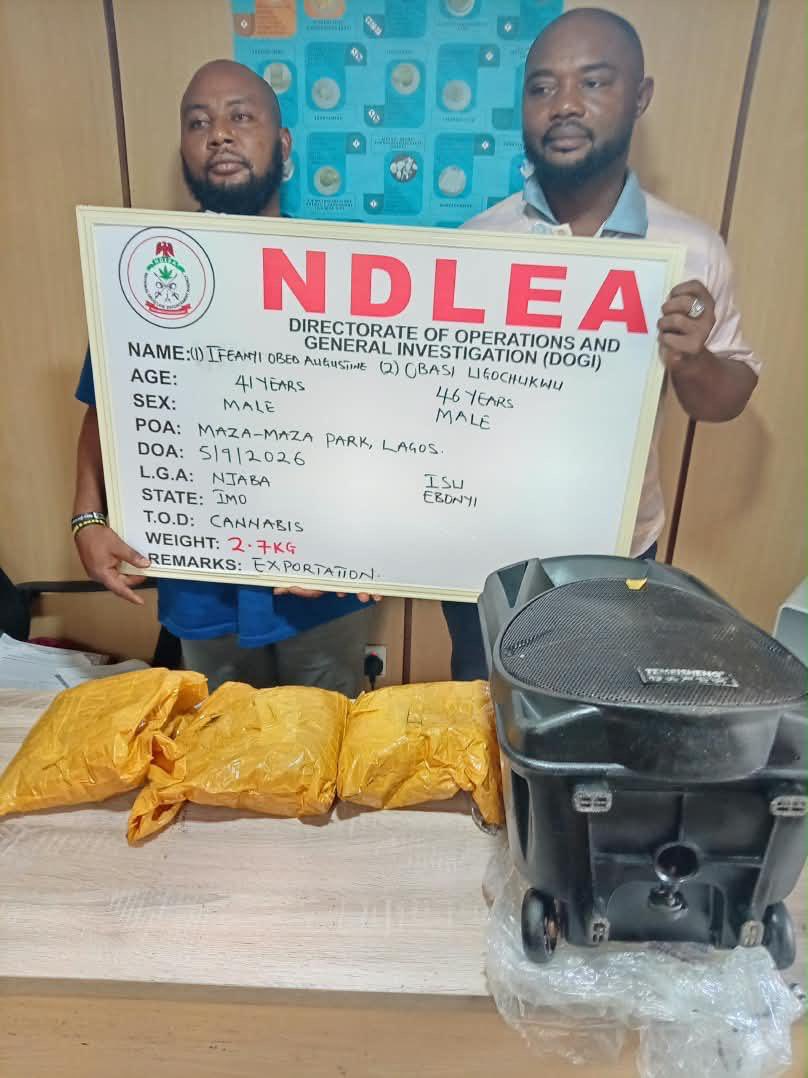 Opiods Speaker - THEWILL NEWS MEDIA Two men stand behind a table, holding an NDLEA certificate board showing seizure details and a large device beside several wrapped packages on the table.
