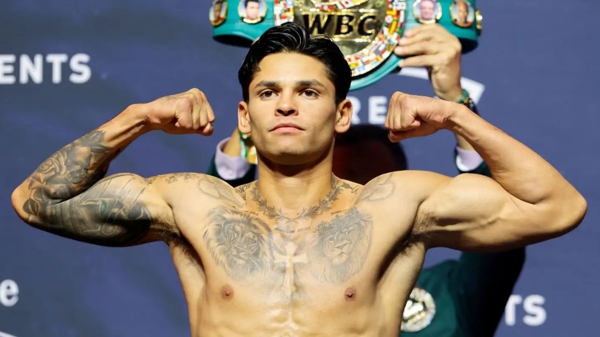Ryan Garcia - THEWILL NEWS MEDIA Boxer with tattoos flexing his biceps on stage, with a WBC championship belt visible behind him.