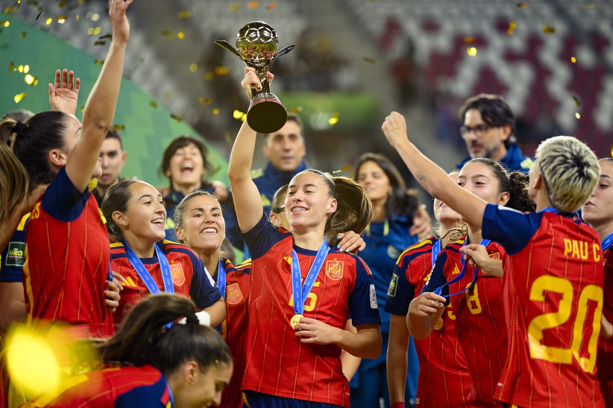 Spain v DPR Korea - FIFA U-20 Womens World Cup Final - THEWILL NEWS MEDIA A girls' sports team in red uniforms celebrate winning a trophy, raising it high with medals around their necks and confetti in the air.