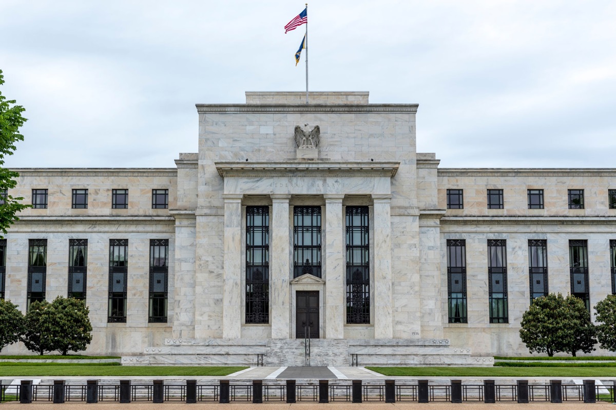 US Federal Reserve building in Washington DC - THEWILL NEWS MEDIA Front view of a marble government building with tall windows, steps, and an American flag atop the central façade.
