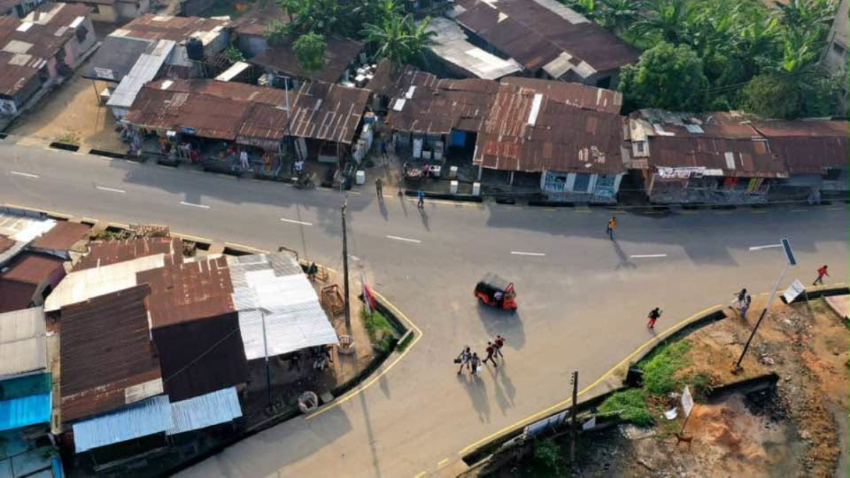 Urua Ekpa Road - THEWILL NEWS MEDIA Aerial view of a hillside neighborhood with rust-colored metal roofs, a curved road, and people walking along the street.