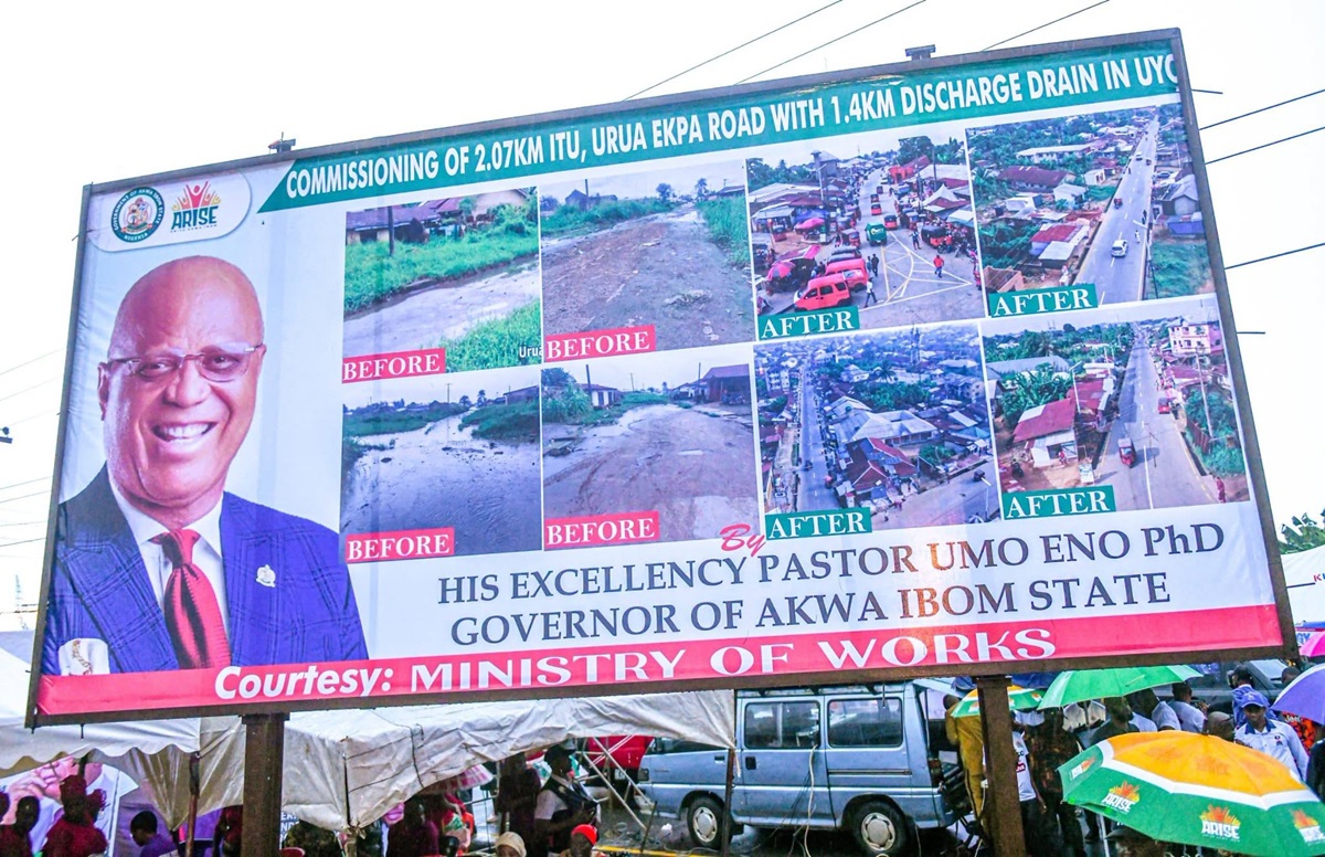 Urua-Ekpa - THEWILL NEWS MEDIA Billboard with a portrait of a smiling man in a suit on the left and a grid of before/after road improvement photos; text proclaims Governor Umo Eno of Akwa Ibom State, courtesy of the Ministry of Works.