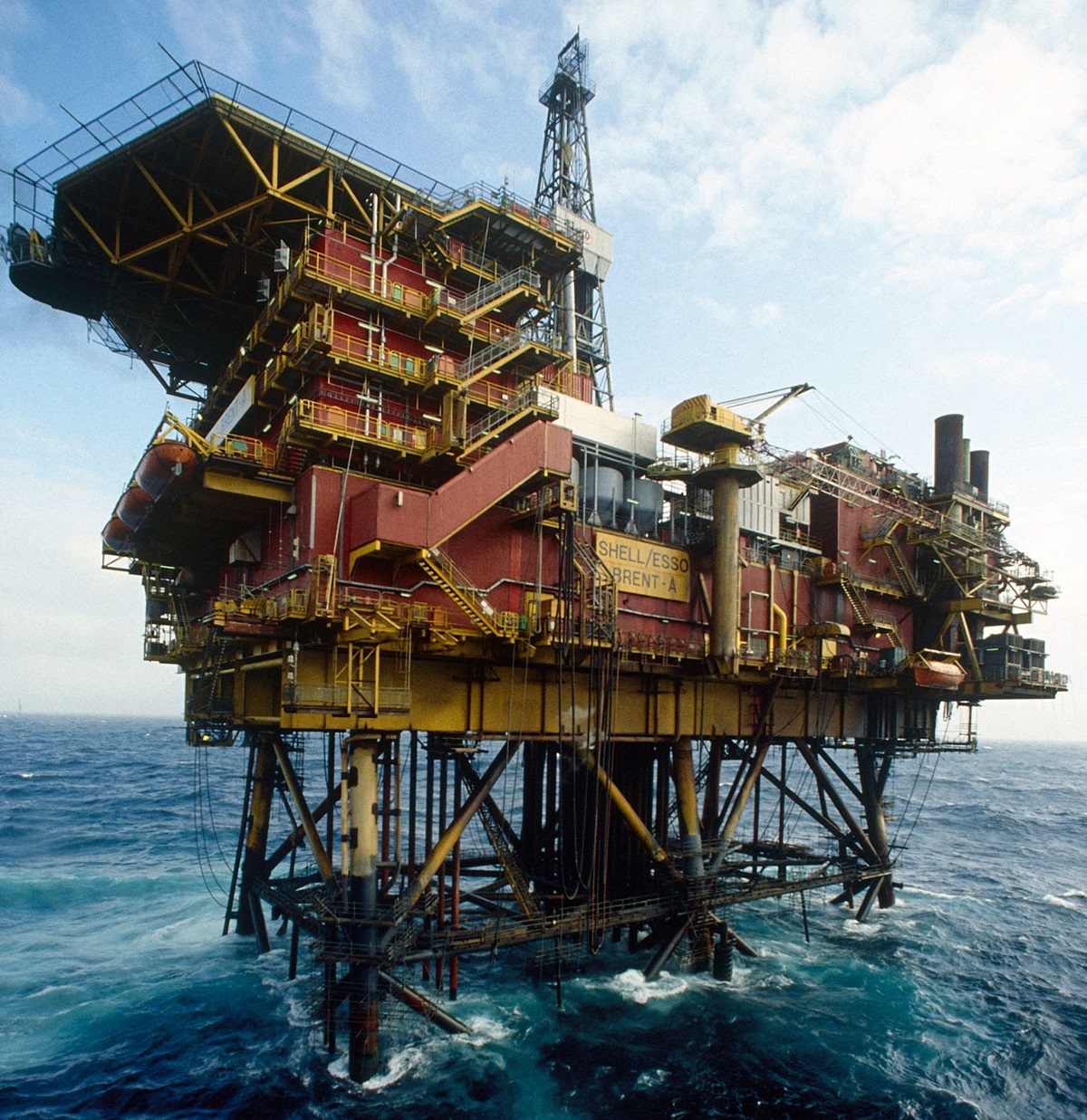 offshore oil production - THEWILL NEWS MEDIA Offshore oil rig towering above blue ocean with yellow-and-red structures and stairways.