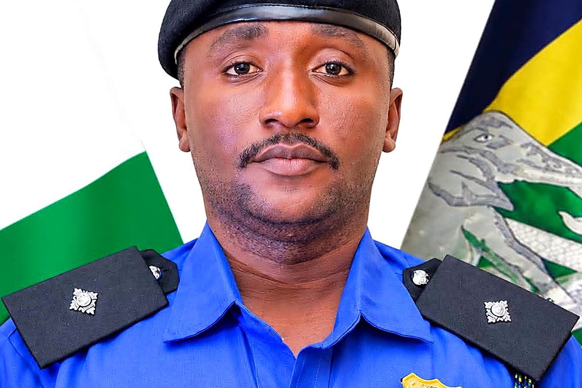 ASP Haruna Rashid Umar Abdullahi - THEWILL NEWS MEDIA Portrait of a police officer in a blue uniform with shoulder epaulets and a black beret, flags in the background