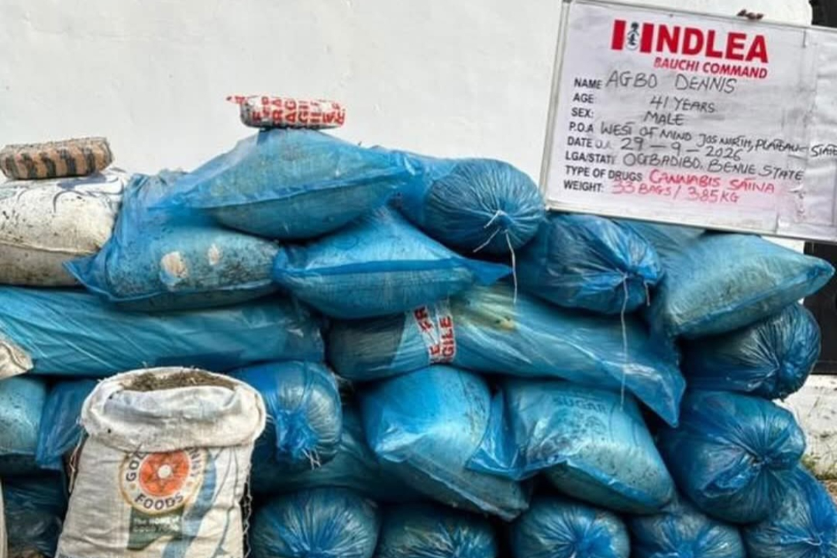Agbo Dennis - THEWILL NEWS MEDIA Pile of blue, tied plastic bags stacked on the ground, with a board displaying drug information in the background.