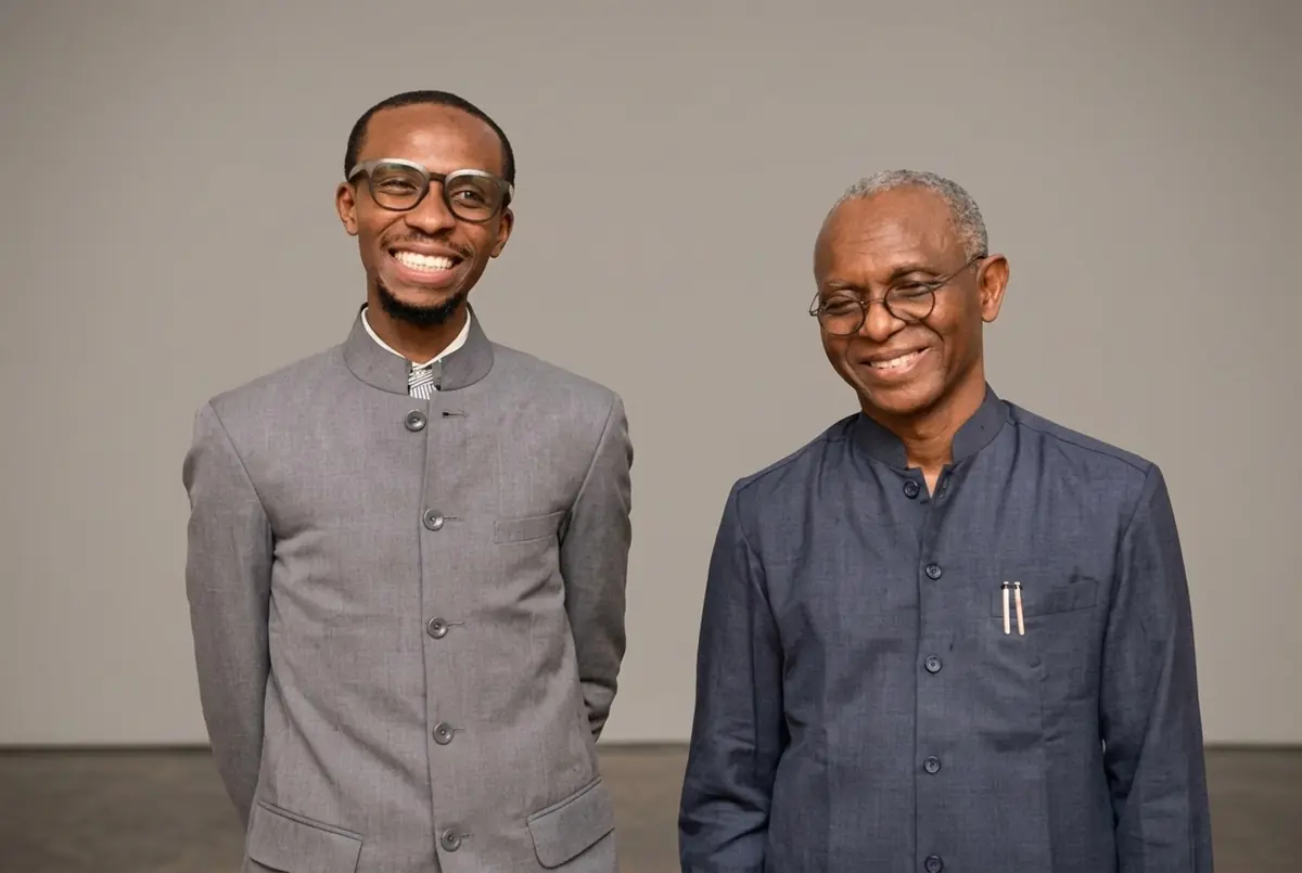 Bello El-Rufai - THEWILL NEWS MEDIA Two men stand side by side, smiling at the camera; one in a light gray mandarin-collar suit and glasses, the other in a dark blue shirt with pens in his chest pocket.