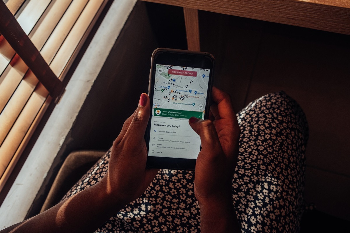 Bolt app - THEWILL NEWS MEDIA Person holding a smartphone displaying a map and navigation screen, viewed from a seated perspective by a patterned dress.