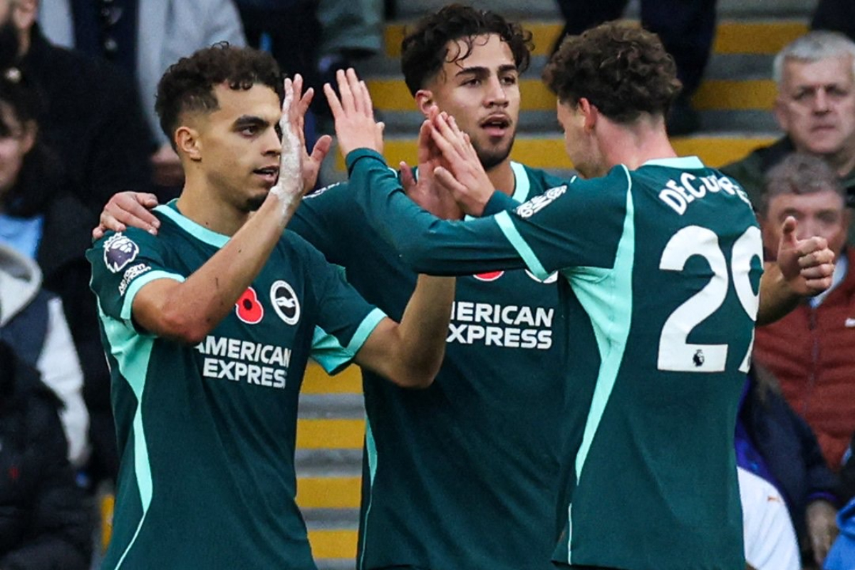 Brighton VS Man City - THEWILL NEWS MEDIA Three football players in teal kits celebrate with high-fives on the pitch, crowd watching in the background. The players wear American Express sponsor and Premier League badges on sleeves.