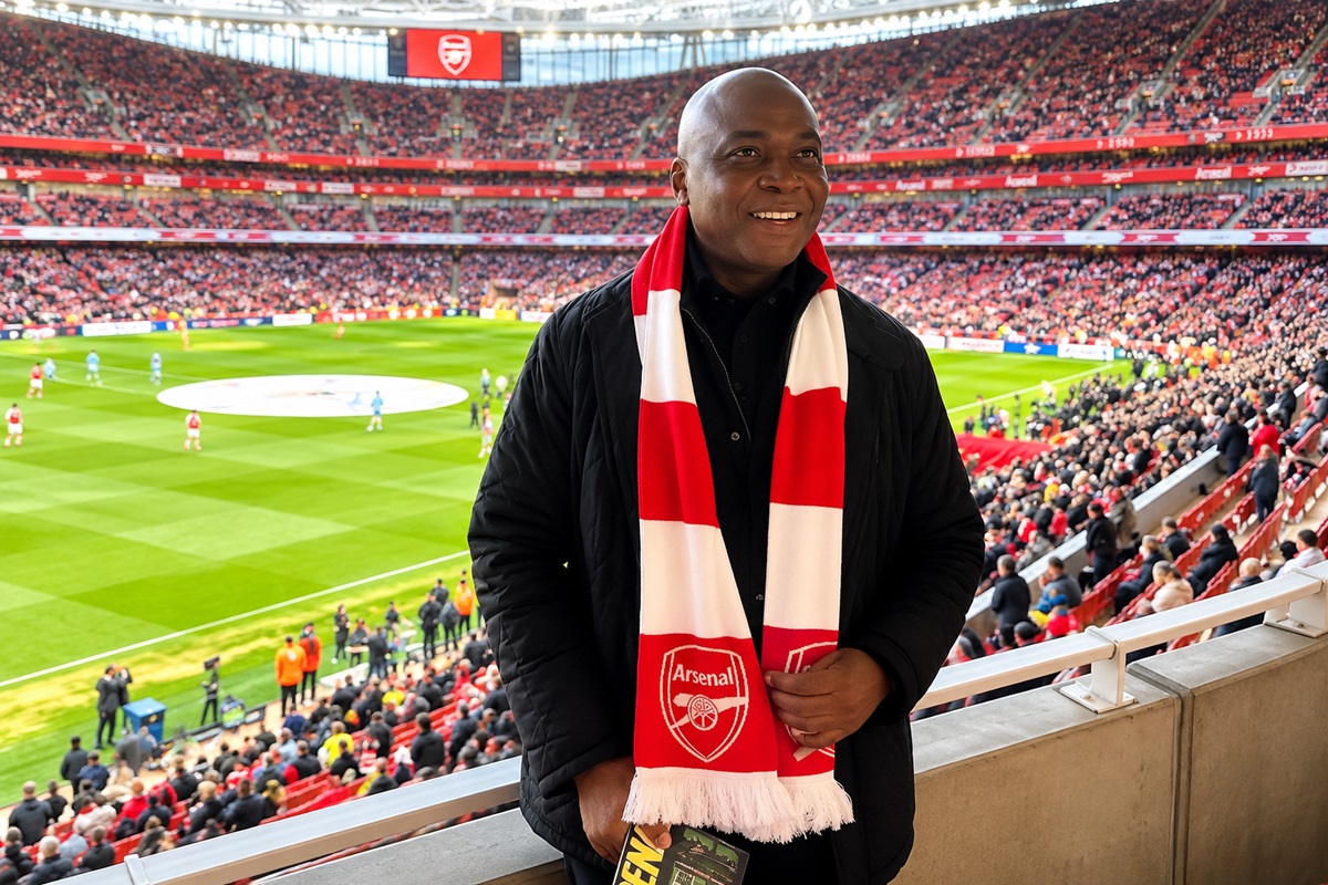 Bukola Saraki - THEWILL NEWS MEDIA Smiling man wearing a red and white Arsenal scarf stands on a balcony over a packed football stadium with a match playing on the field behind him.
