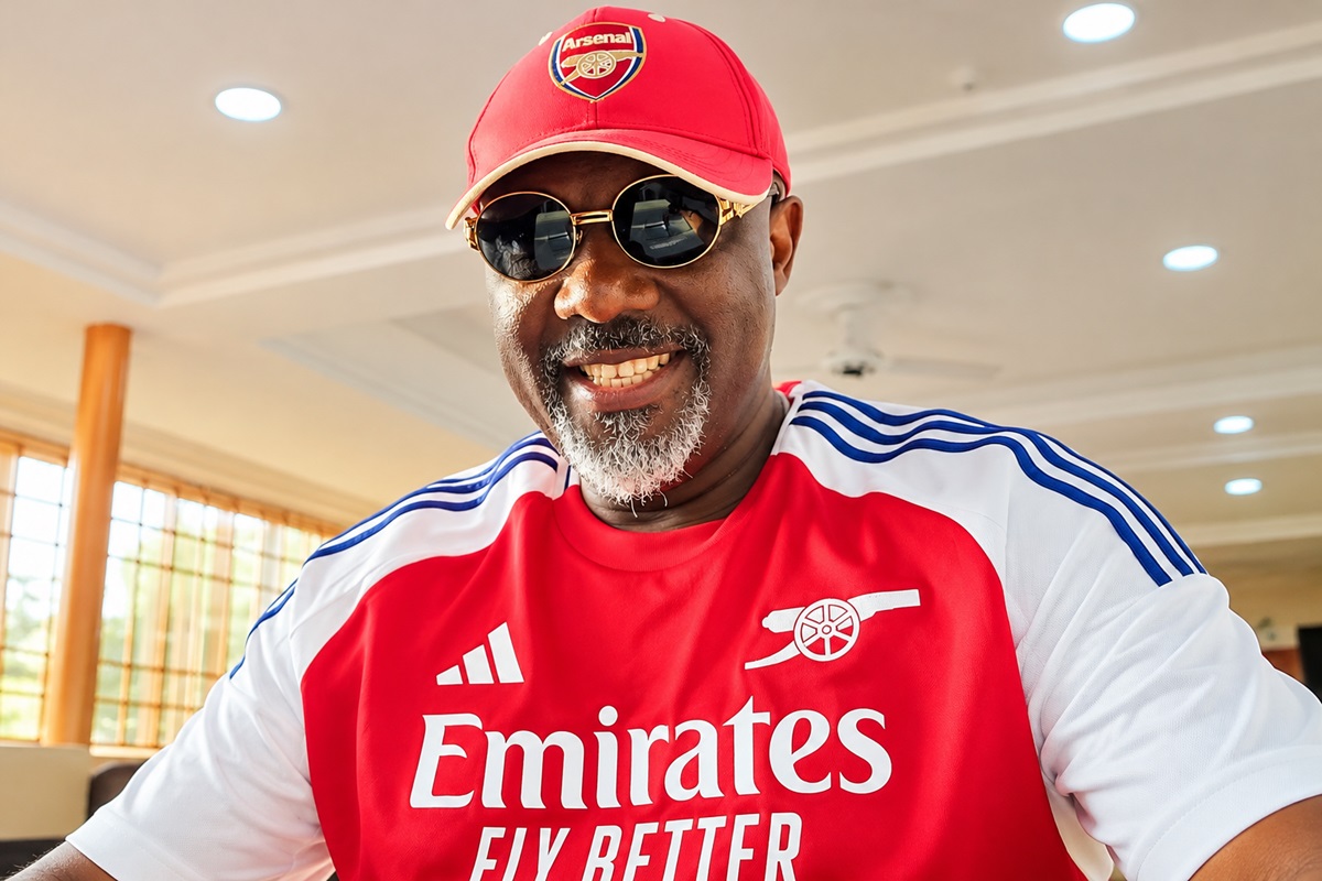 Dino Melaye - THEWILL NEWS MEDIA Smiling man wearing a red Arsenal jersey and cap with sunglasses indoors, taking a selfie.