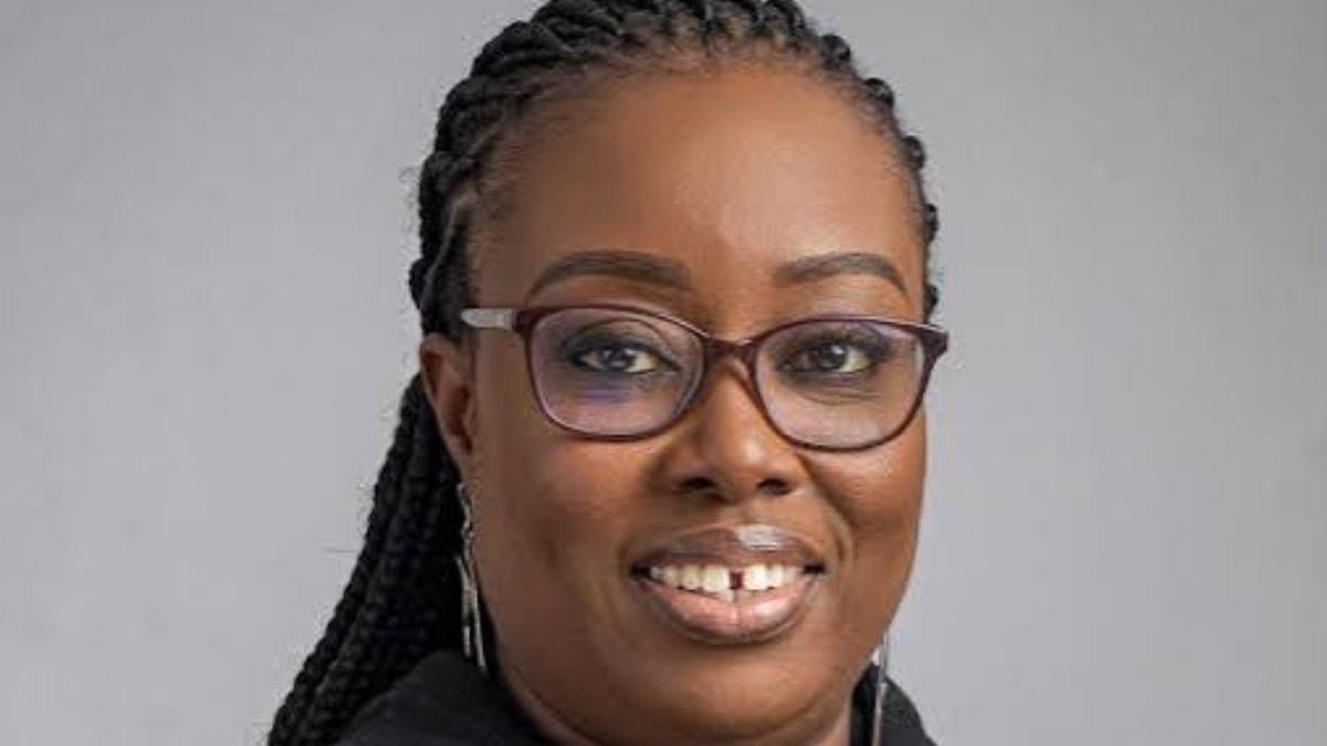 Eduofon Japhet - THEWILL NEWS MEDIA Portrait of a smiling Black woman with braided hair and glasses against a gray background, facing the camera.