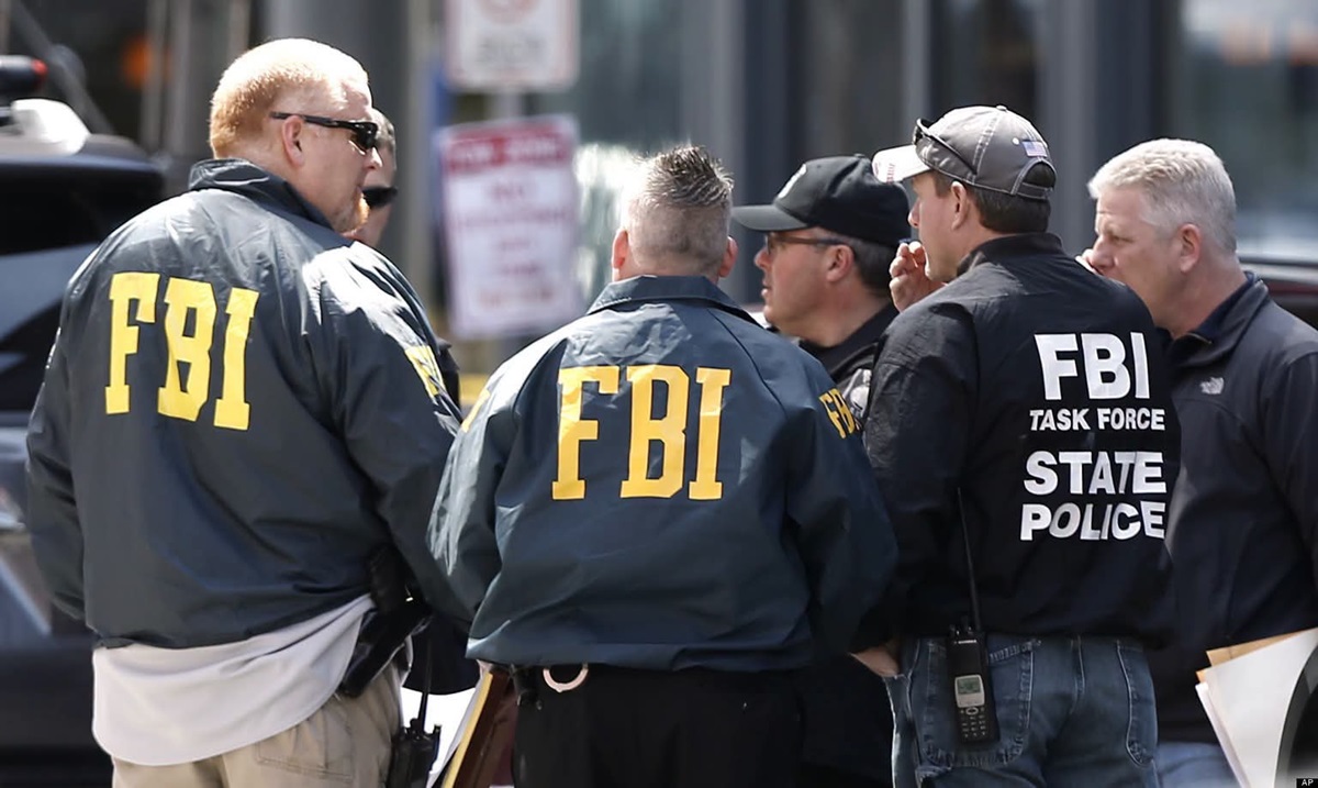 FBI - THEWILL NEWS MEDIA A group of FBI agents in dark jackets with large yellow FBI letters gather in a street, discussing a case outside a building.