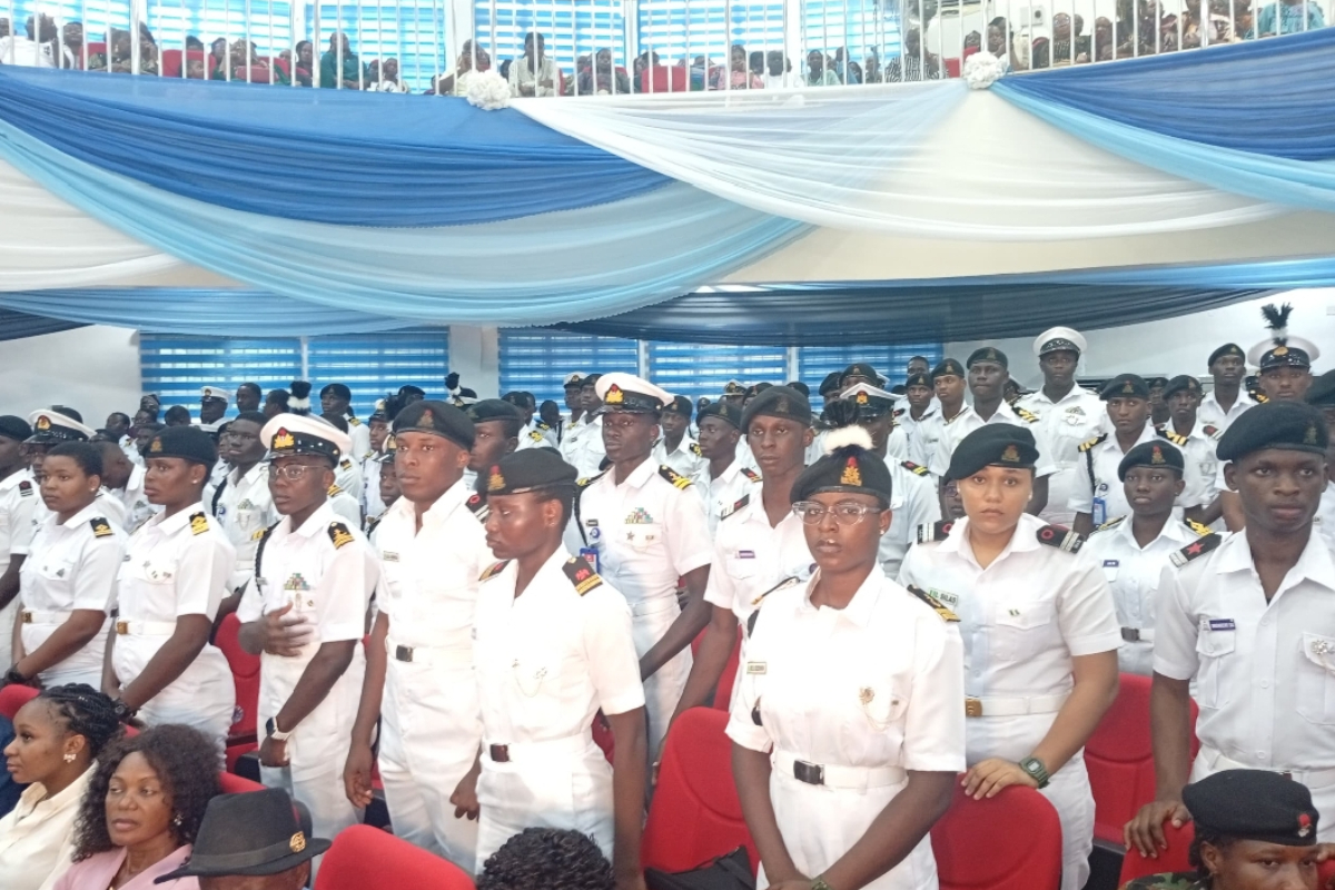 FG Targets Global Maritime Jobs - THEWILL NEWS MEDIA Group of uniformed naval officers standing at attention in a ceremony hall, with red chairs and blue-white drapes overhead and spectators in the background.