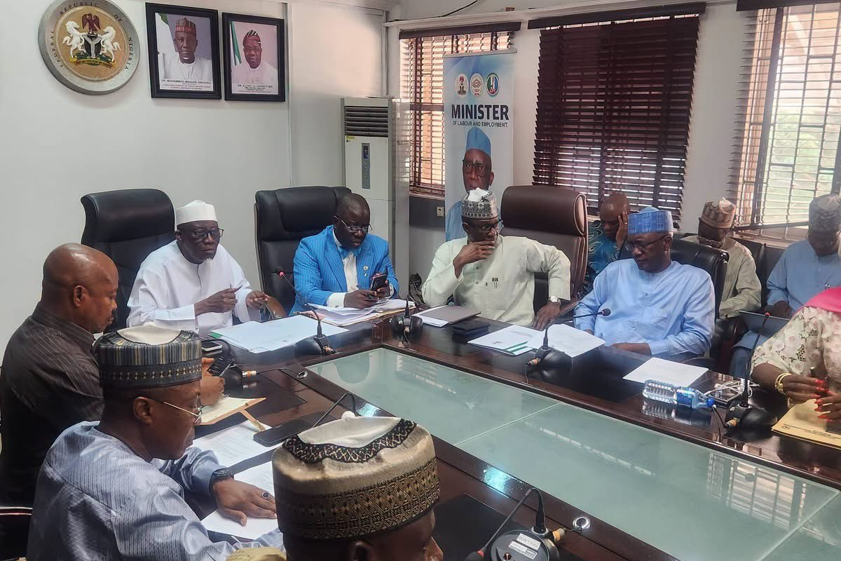 FG and Lbour in meeting - THEWILL NEWS MEDIA Officials in a conference room around a long glass table reviewing documents, a banner reading 'MINISTER' in the background.