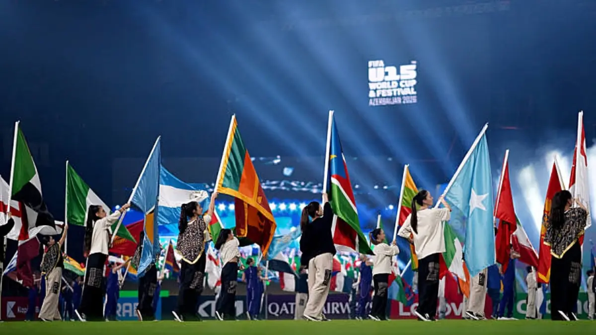 FIFA U15 World Cup Festival - THEWILL NEWS MEDIA Diverse performers on a stadium field waving international flags during a World Cup opening ceremony drenched in blue lights.