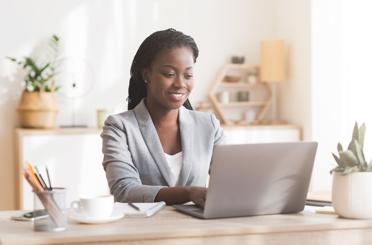 Founders review equity terms - THEWILL NEWS MEDIA Professional woman in a gray blazer typing on a laptop at a tidy home office desk with plants nearby.