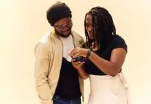 Two friends look at a smartphone together, the woman showing something on the screen to the man wearing a beanie.