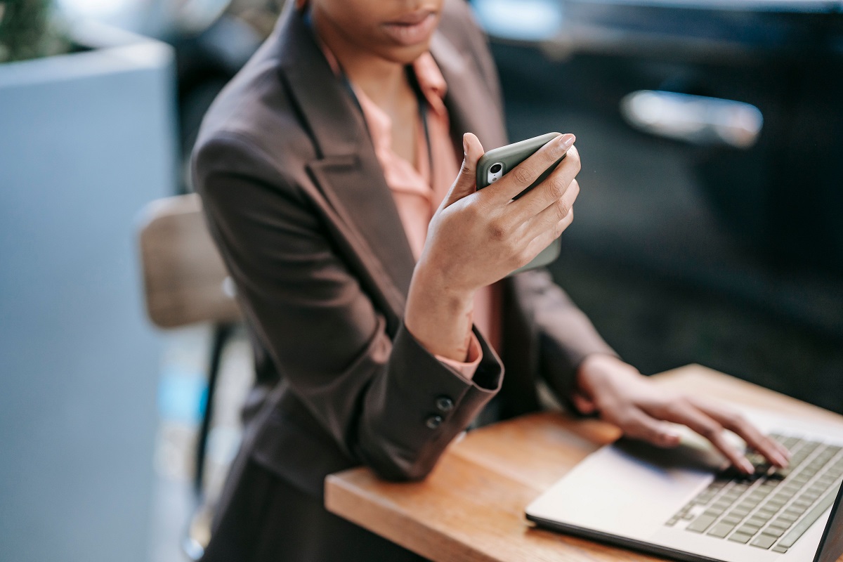 A woman uses a smartphone while working on a laptop - THEWILL NEWS MEDIA SafeTech Africa
