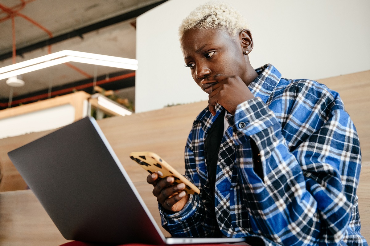 Woman checks her phone beside an open laptop - THEWILL NEWS MEDIA SafeTech Africa