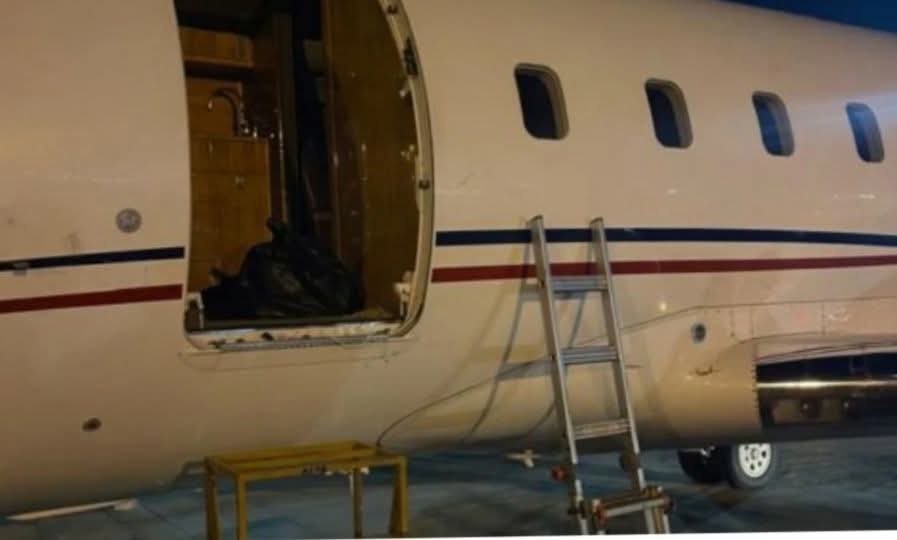 Airplane with open passenger door, a right-side airstair ladder, and a yellow maintenance table nearby on tarmac at night/sunset.