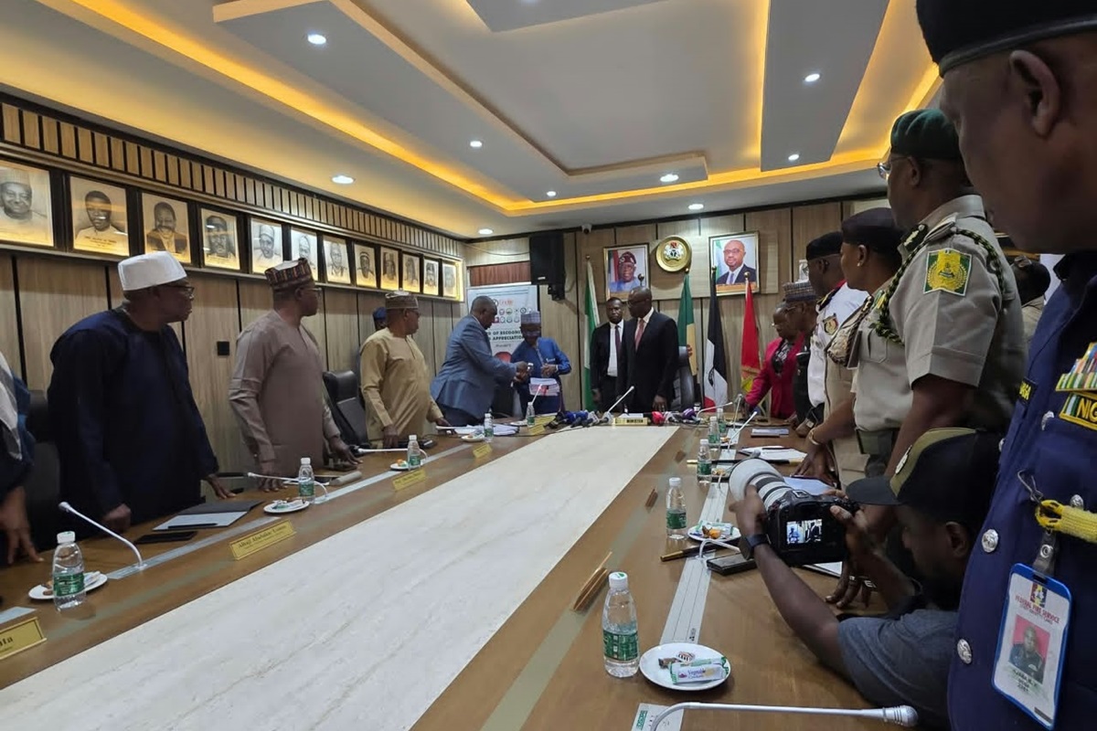 Investigative committee on Niger NSCDC Incidents - THEWILL NEWS MEDIA Officials in traditional and formal attire stand along a long conference table as they shake hands in a ceremonial meeting room setting.