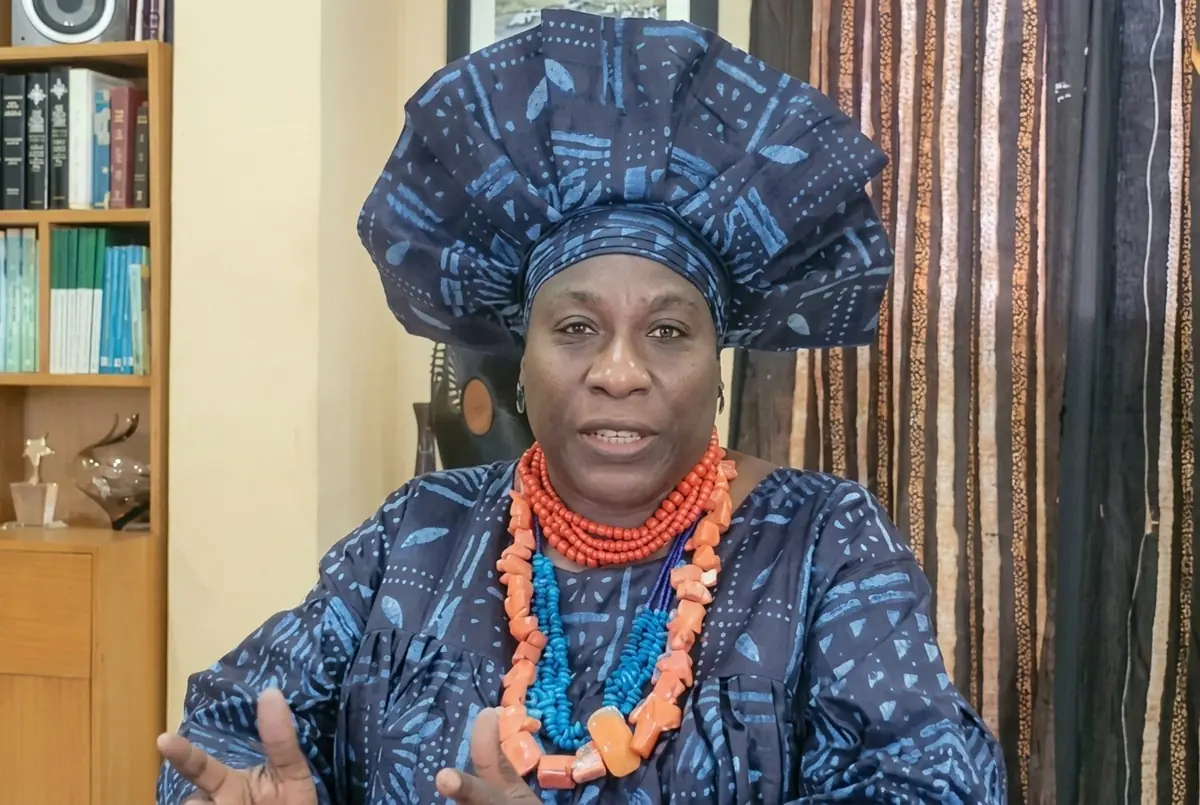 Iyabo Obasanjo - THEWILL NEWS MEDIA Woman in blue patterned traditional attire with a large head wrap and coral-bead necklaces, speaking to the camera indoors.