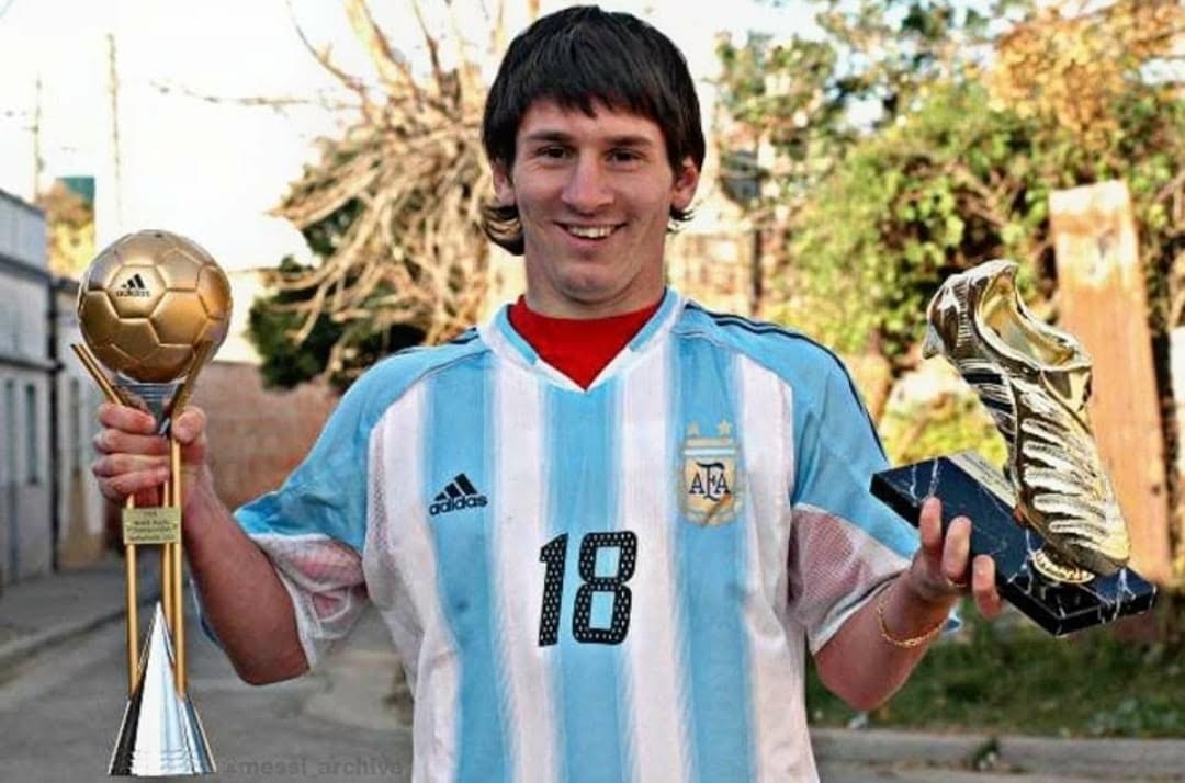 Lionel Messi - THEWILL NEWS MEDIA Young man in a light-blue Argentina jersey holding a trophy in each hand, smiling outdoors.