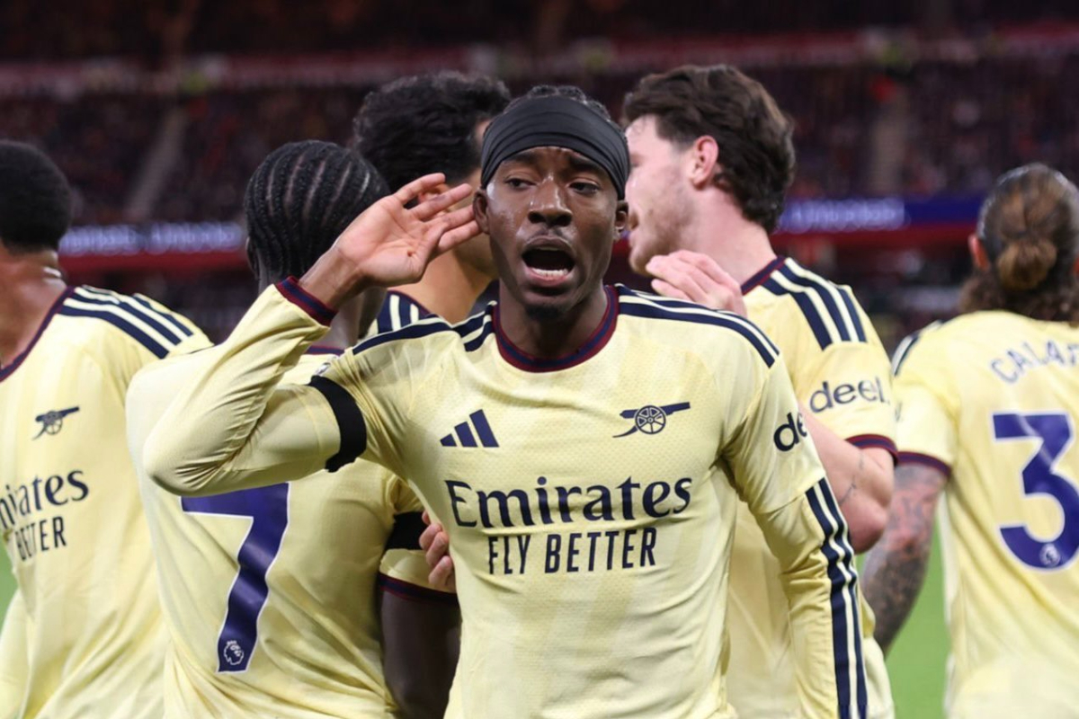 Madueke - THEWILL NEWS MEDIA Soccer players in pale yellow Arsenal kits celebrate on the field, with the central forward gesturing near his ear as teammates hug him.