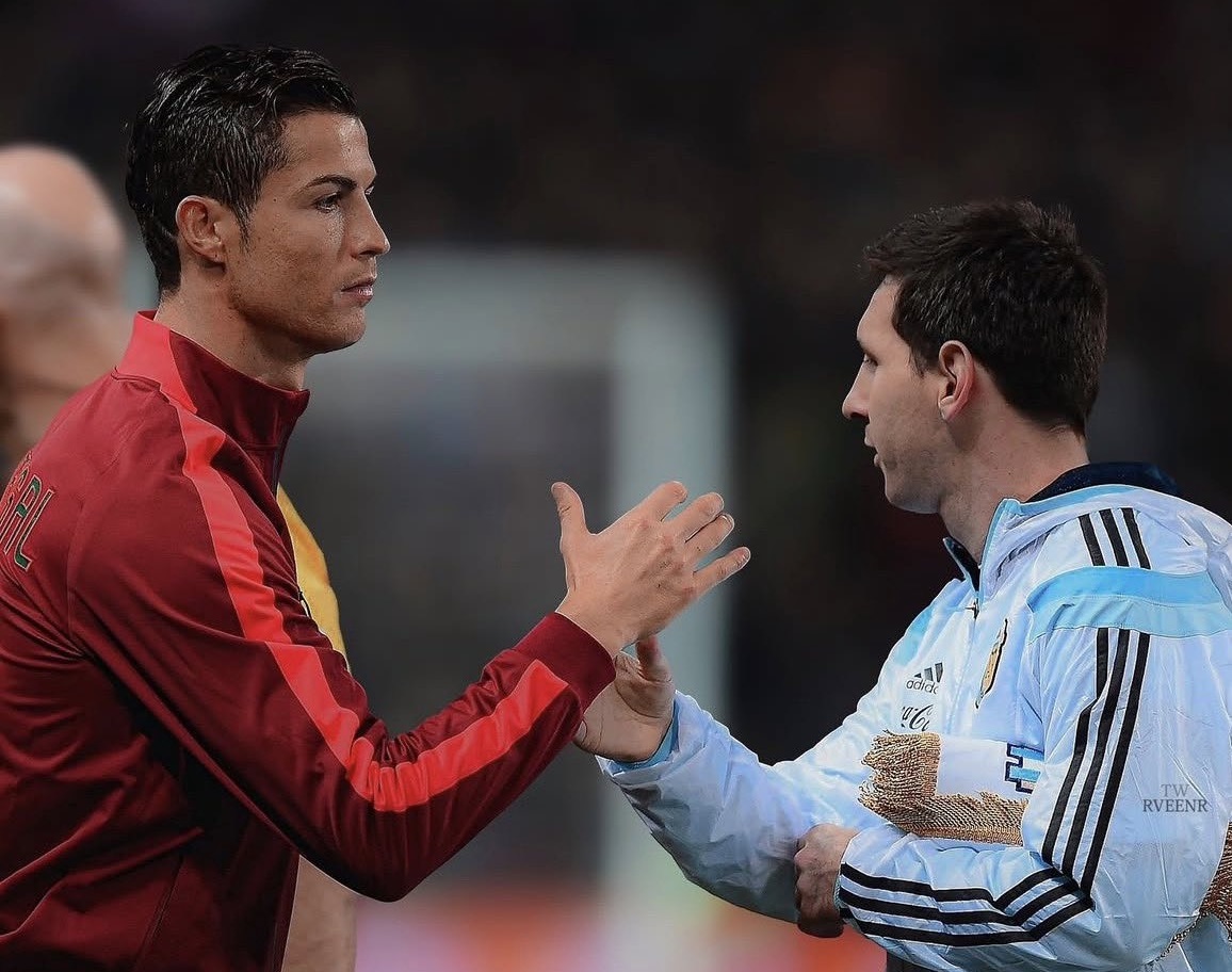 Messi and Ronaldo - THEWILL NEWS MEDIA Two male soccer players greet each other with a handshake on the field, one in red and the other in light blue.