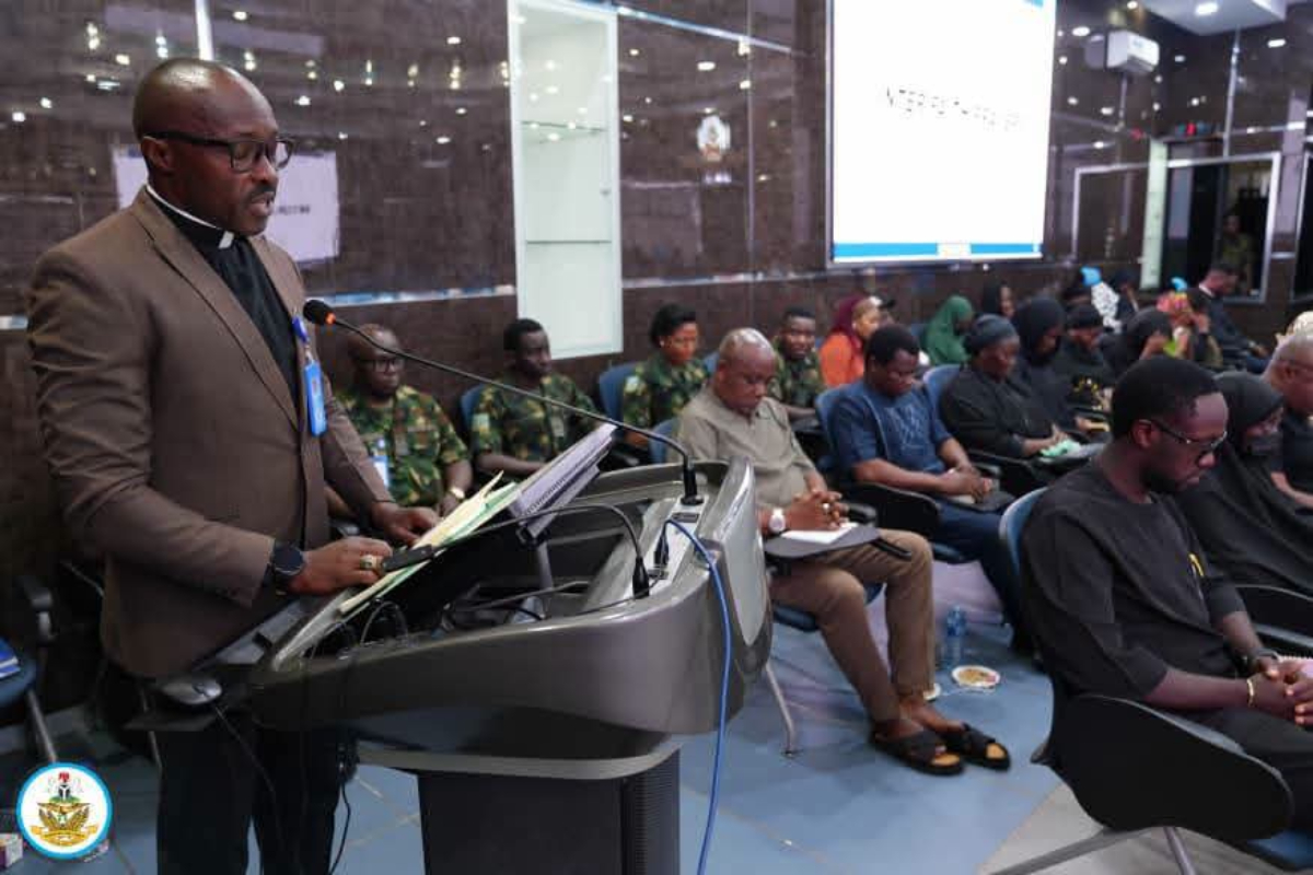 NAF - THEWILL NEWS MEDIA Man in a brown suit speaks at a podium in a conference room, addressing an audience seated in rows.