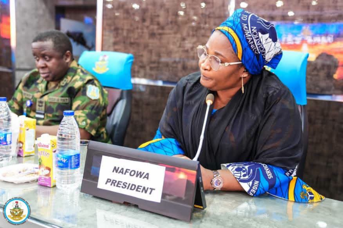 NAFOWA President - THEWILL NEWS MEDIA NAFOWA president seated at a panel table with a microphone, wearing a blue patterned headwrap and glasses, beverages visible nearby