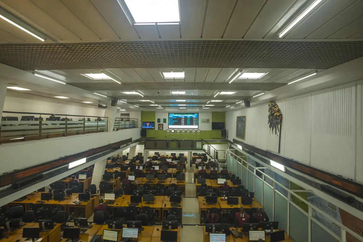 NGX trading floor - THEWILL NEWS MEDIA A large control room filled with rows of desks and computer monitors, staff at work under bright ceiling lights with a big screen at the front.