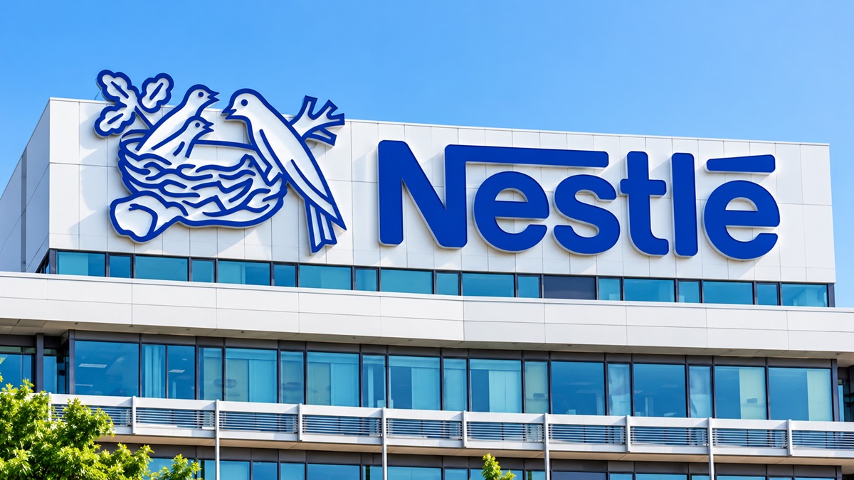 Nestlé Headquarters - THEWILL NEWS MEDIA Exterior view of a Nestlé office building with the blue Nestlé logo and nest illustration on a white facade, under a clear blue sky.