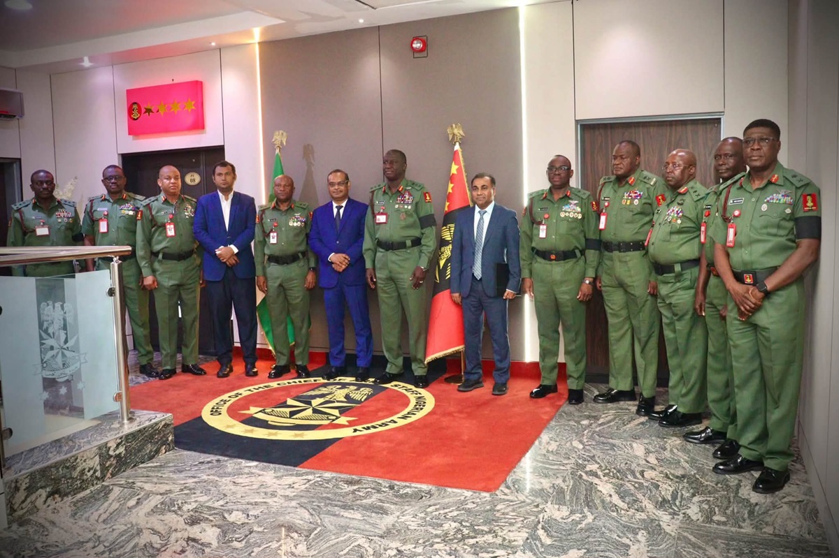 Nigeria Bangladesh Deepen Defence Ties - THEWILL NEWS MEDIA Group of uniformed military officers and two men in suits posing for a photo in a formal hallway with national flags and a circular emblemed rug.