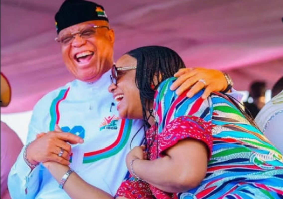 Pastor Umo Eno and his daughter - THEWILL NEWS MEDIA Two people sharing a joyful hug and a big laugh at a festive gathering, under a pink canopy.