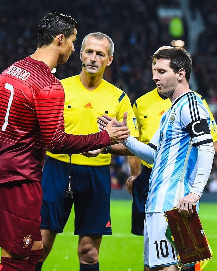 Ronaldo and Messi - THEWILL NEWS MEDIA Portugal's Cristiano Ronaldo (jersey #7) shakes hands with Lionel Messi from Argentina on the field, with a referee between them.