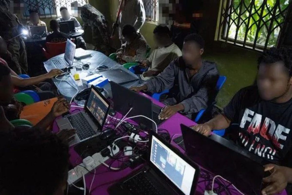 Scammer in Ghana - THEWILL NEWS MEDIA Group of people gathered around a table with multiple laptops and cables, working together in a tech workshop.